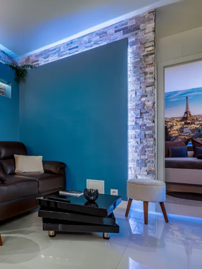 Après travaux : le même salon, mur bleu, parement en pierre éclairé et sol brillant